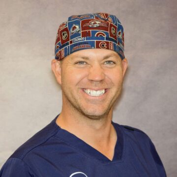 A smiling man wearing scrubs and a patterned surgical cap.